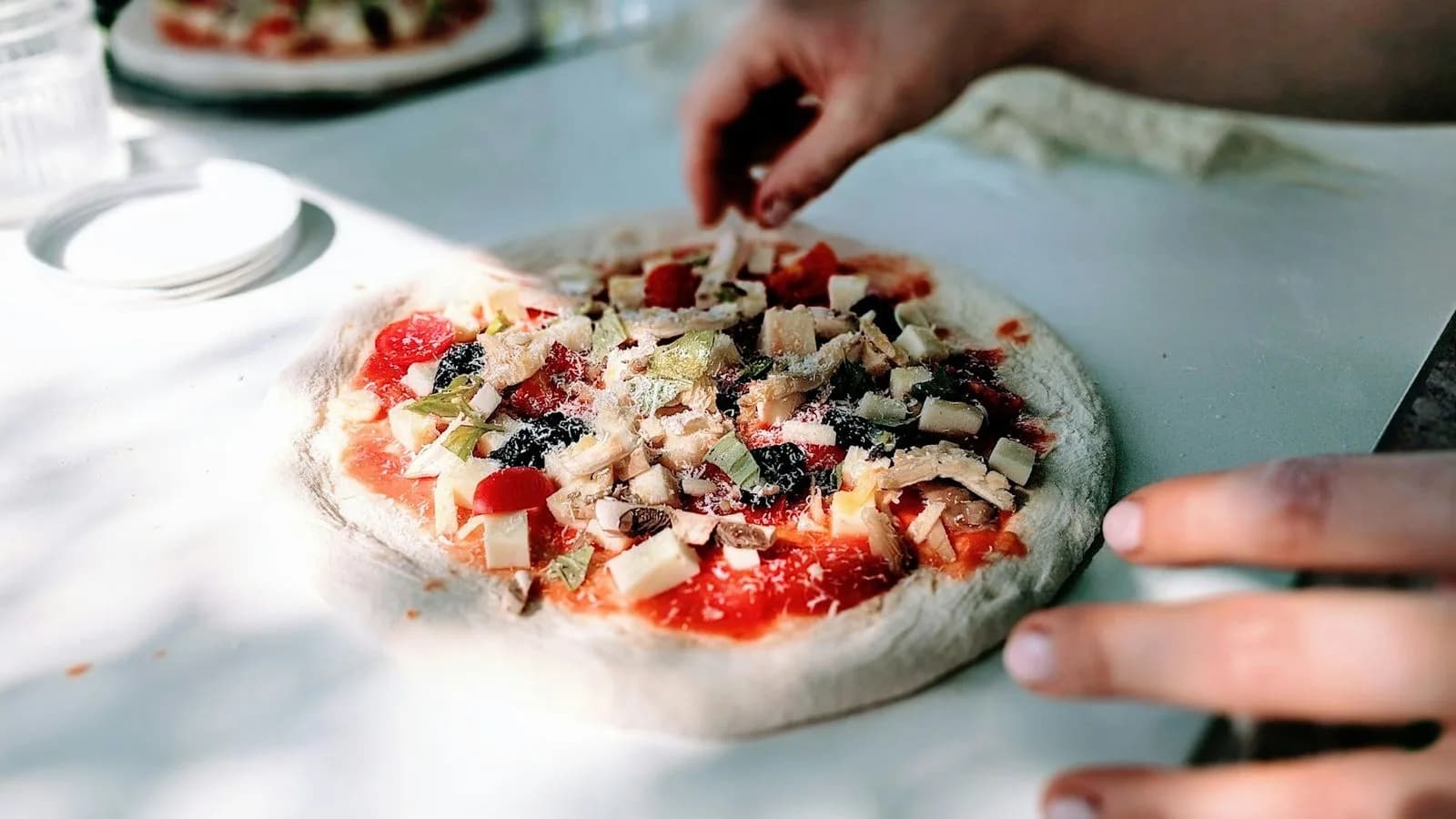 Hands preparing a pizza with fresh toppings. Illustrative photo.