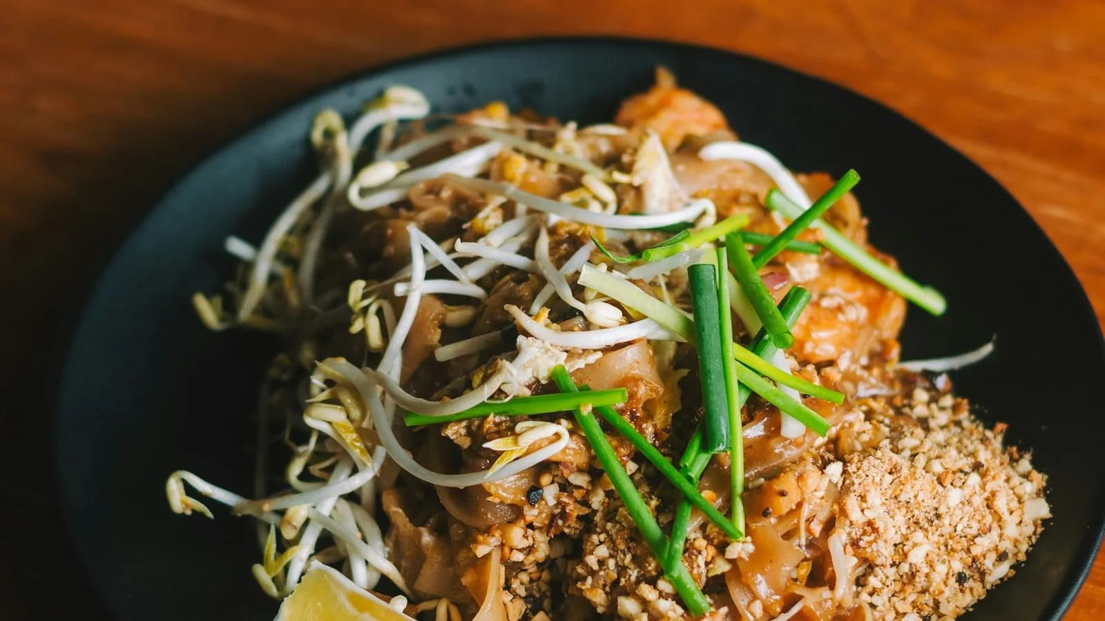 Pad Thai noodles with bean sprouts, herbs and peanuts on a dark plate. Illustrative photo.