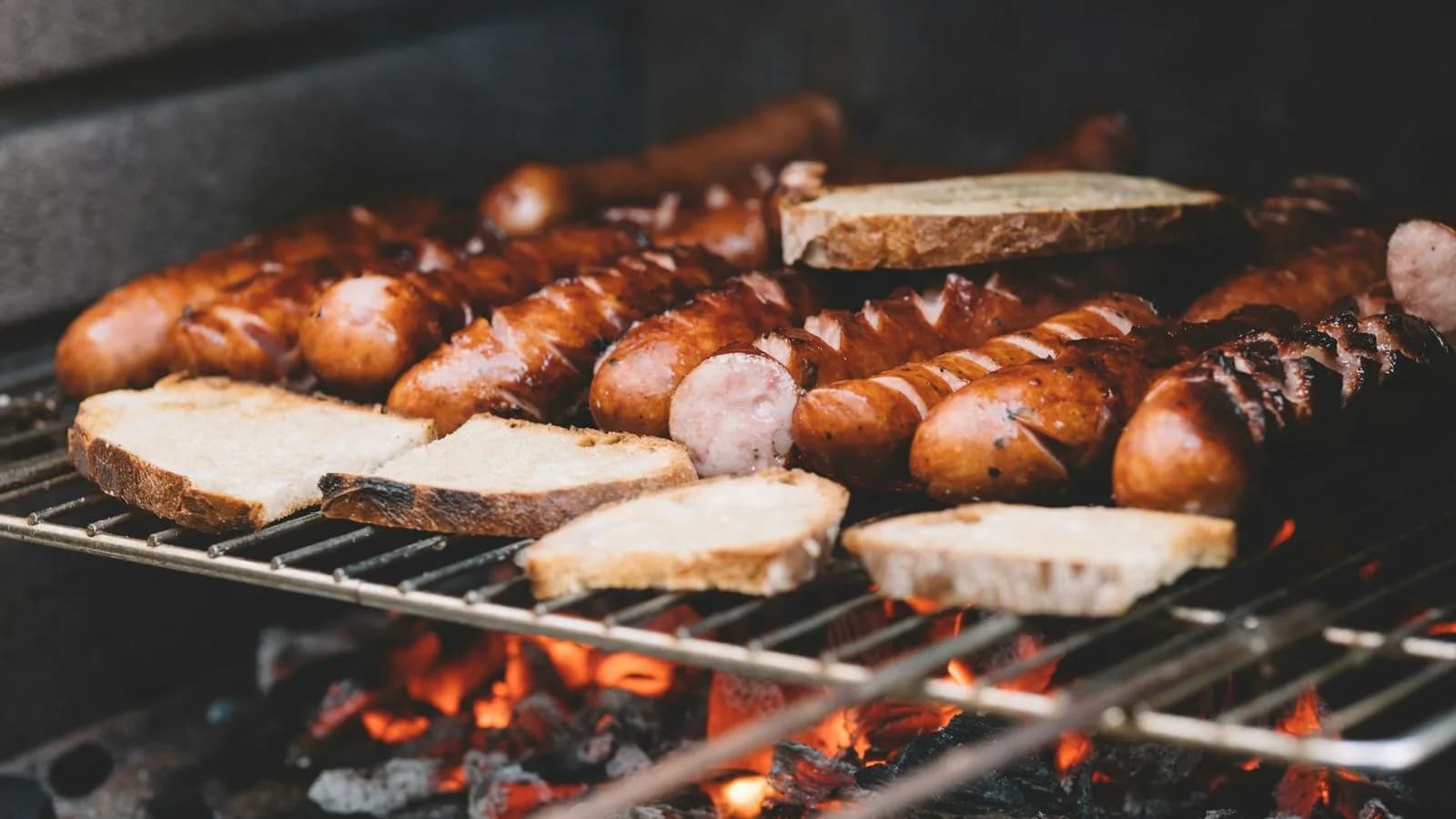 Sausages and bread cooking over a charcoal grill. Illustrative photo.